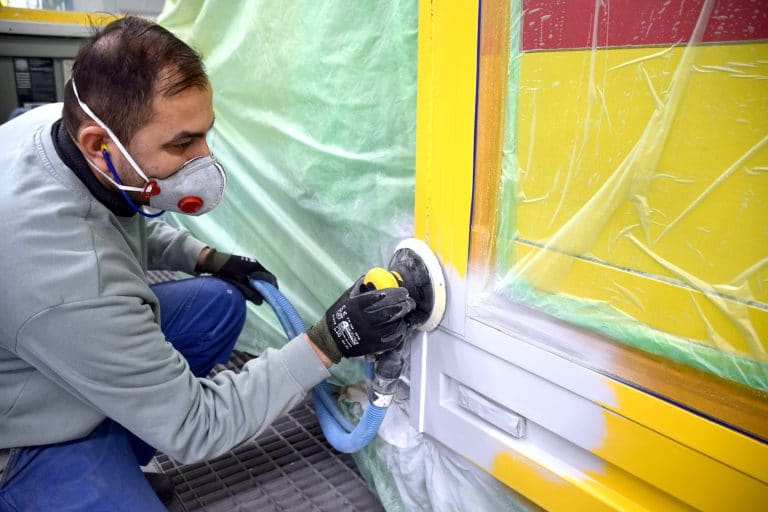 Mitarbeiter schleift mit Exzenterschleifer eine vorbereitete Fahrzeugfläche vor dem Lackieren ab.