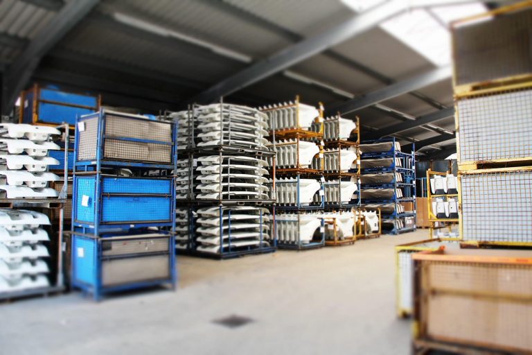 Lagerhalle mit gestapelten Gitterboxen und lackierten Fahrzeugteilen zur Zwischenlagerung bei Diebald Lackierung.